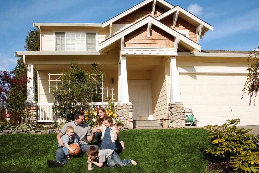 Family of five sitting on the front lawn of a two-storey craftsman house