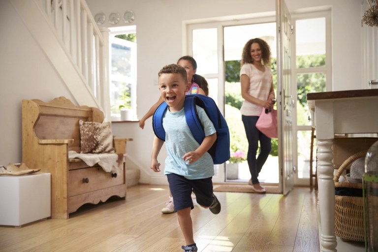 Young boy with a backpack running into the house as his mother follows