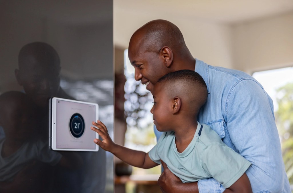 Man holding a young boy who touches a wall-mounted smart thermostat display