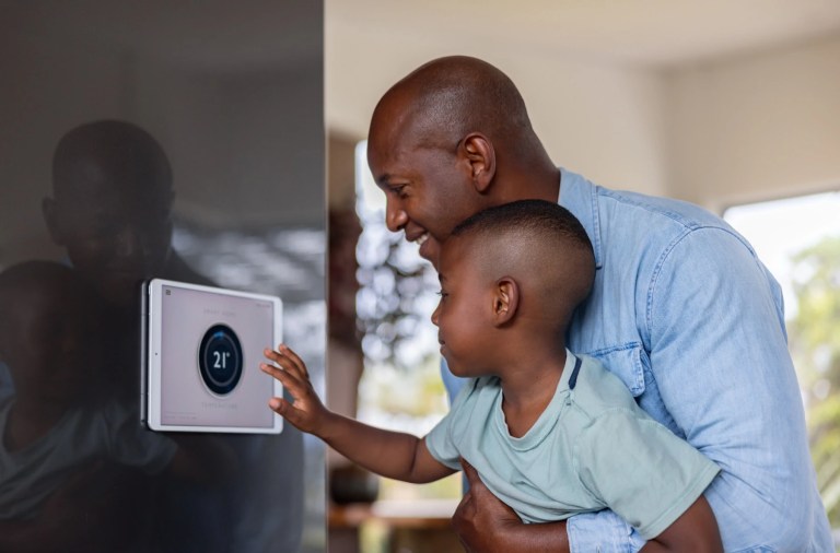 Man holding a young boy who touches a wall-mounted smart thermostat display