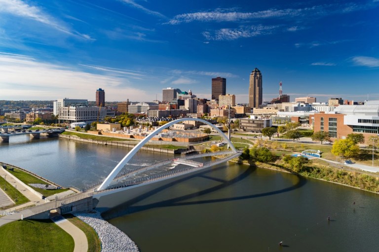 Aerial view of a riverside city skyline with a white arched pedestrian bridge