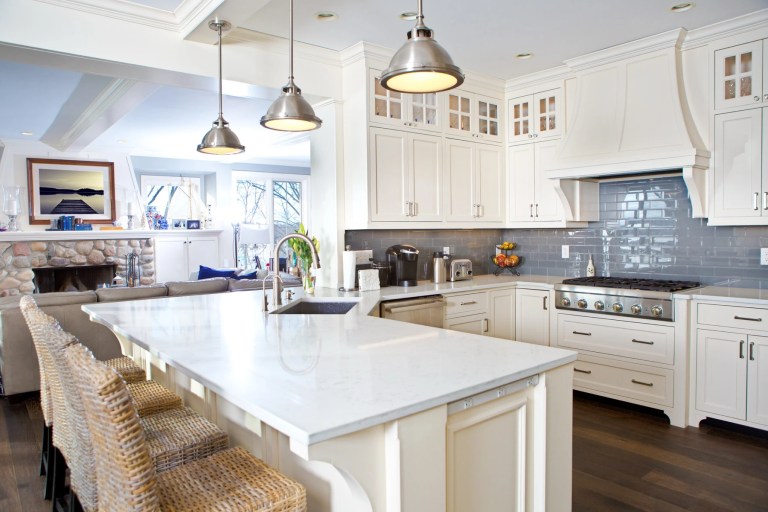 Bright white kitchen with a marble island, pendant lights and a gas range