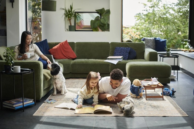 Man and toddler reading a picture book on a rug with a woman and dog nearby