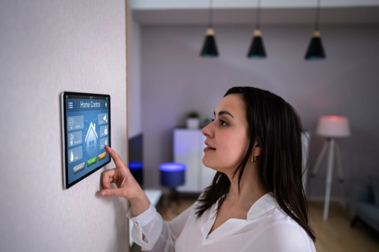 Woman touching a wall-mounted smart home control panel showing lighting and temperature icons