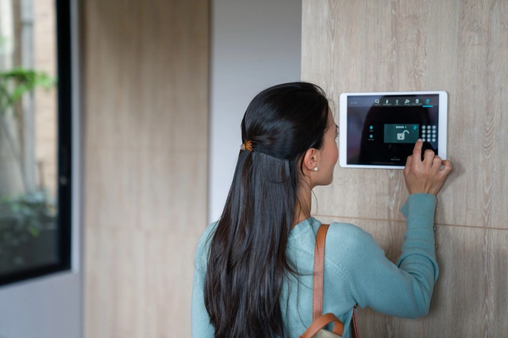 Woman entering a code on a wall-mounted home security panel before leaving