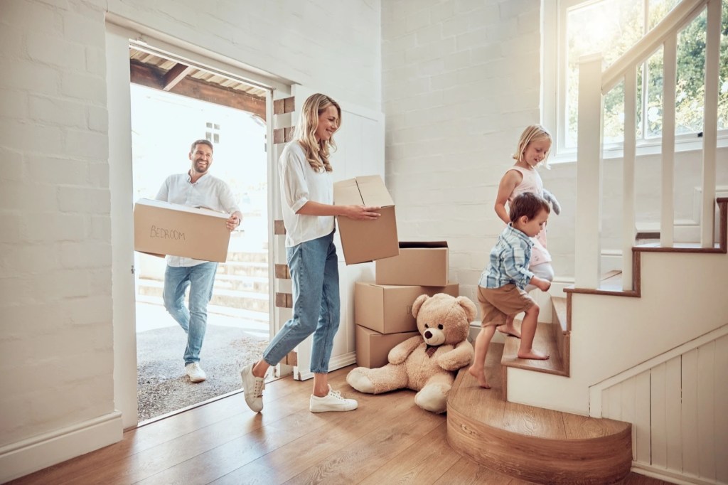 Family carrying moving boxes into a bright new home with children on the stairs
