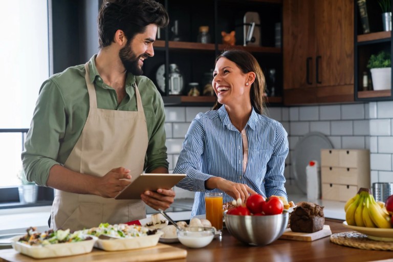 Man and woman laughing together over fresh food at a kitchen counter