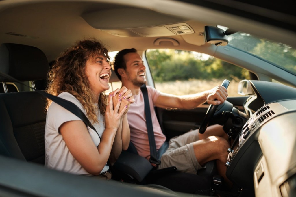 Couple laughing in a car with the man driving and the window down