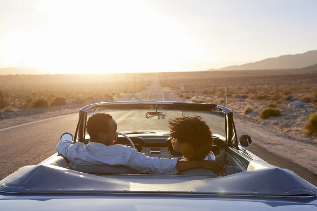 Couple driving a convertible down an open desert highway at sunset