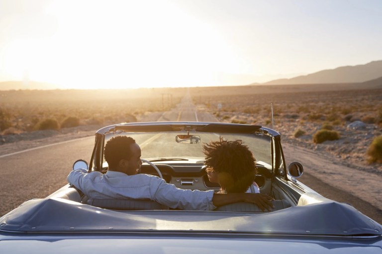 Couple driving a convertible down an open desert highway at sunset