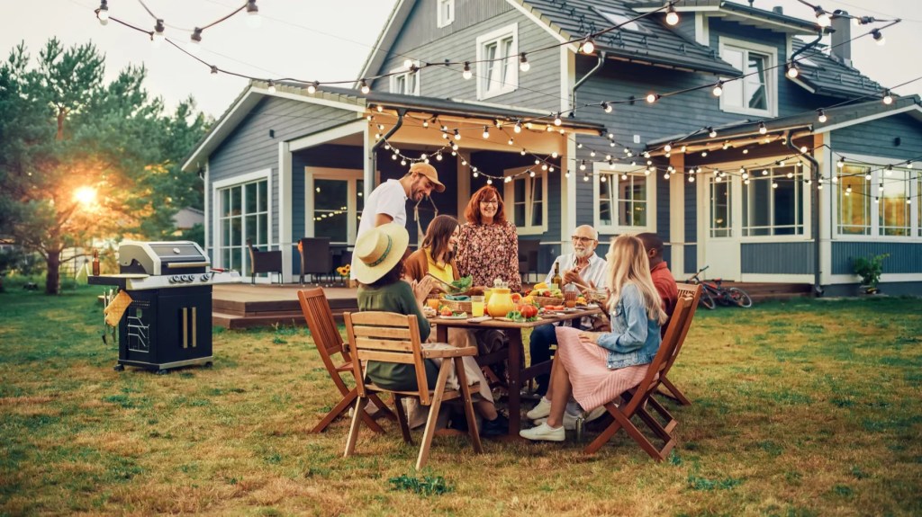 Family and friends gathered at a garden table under string lights outside a house