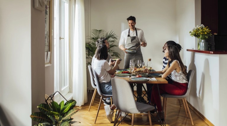 Man serving food to friends around a dining table in a bright apartment