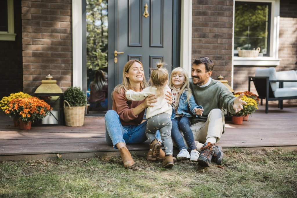 Family with two young children sitting on the front porch steps of a brick house