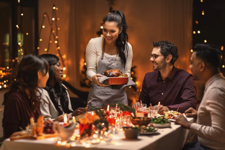 Woman bringing a roast to a candlelit holiday dinner table with friends