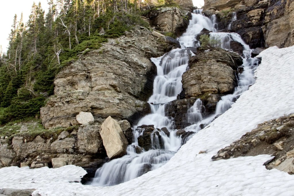 Meltwater cascading down a rocky mountainside beside a bank of snow