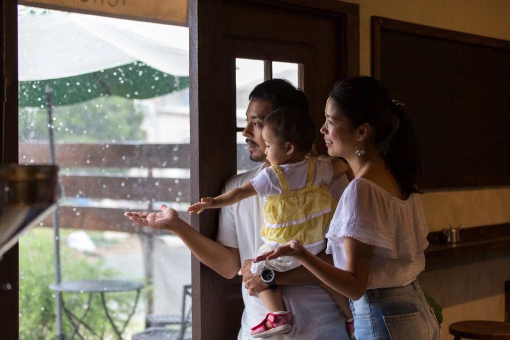 Family with a toddler holding their hands out to rain from a doorway