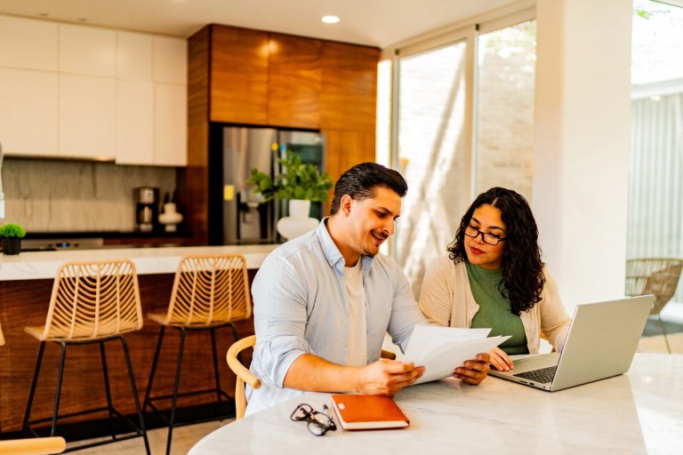 Man and woman reviewing paperwork at a kitchen table with a laptop