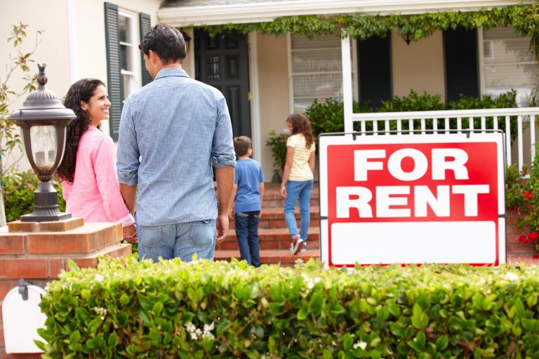 Family walking up to a house with a large For Rent sign in the front garden