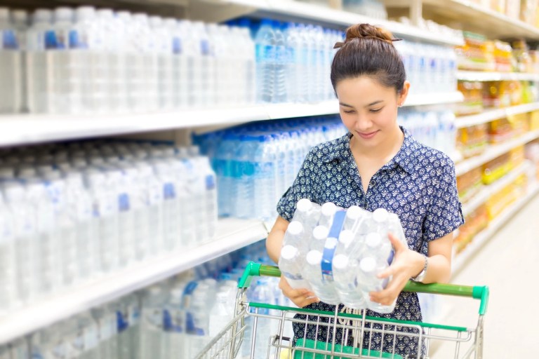 Woman choosing a pack of bottled water in a supermarket aisle