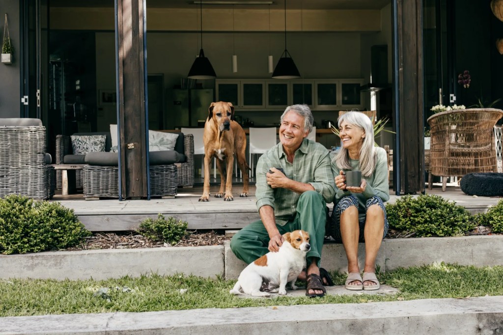 Older couple with two dogs relaxing with coffee on their back patio steps